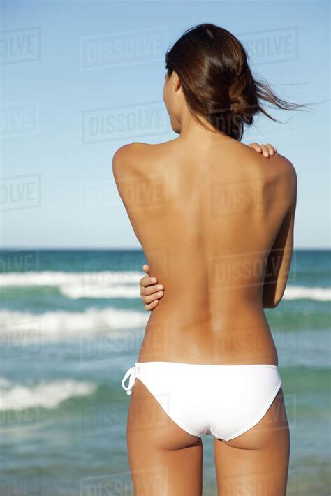 Semi Naked Woman In Bikini Bottom Hugging Self By Ocean Rear View