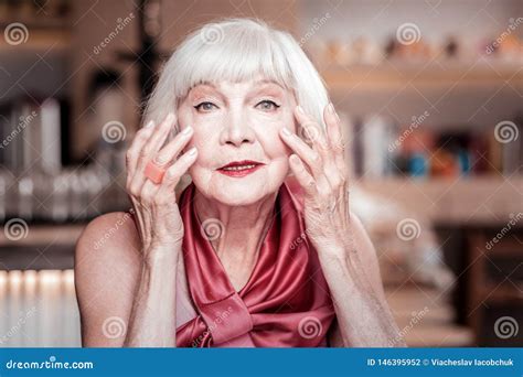 Grey Haired Old Lady In Pink Top And Bright Makeup Treating Wrinkles