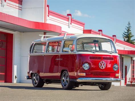 A Red And White Vw Bus Parked In Front Of A Building Next To A Parking Lot