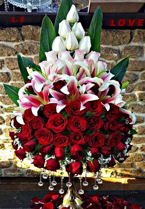Red Roses And White Lilies In A Vase On A Table Next To A Brick Wall