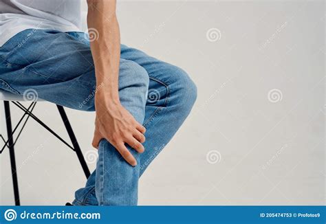 Man In Jeans Sitting On A Chair And Touching His Leg With His Hands Cropped View Stock Image