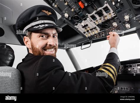 Cheerful Pilot In Cap Reaching Overhead Panel With Set Of Switches In