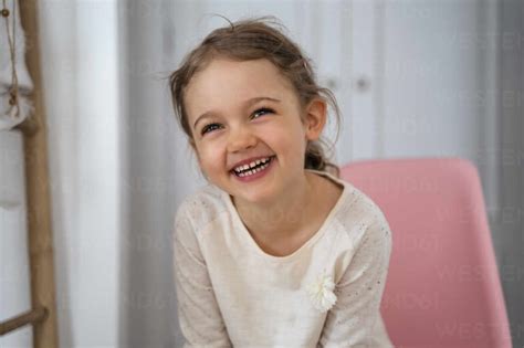 Happy Cute Girl Sitting On Chair At Home Stock Photo