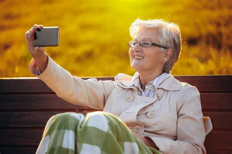 an older woman taking selfies while sitting on the bench in the colorful park in the autumn