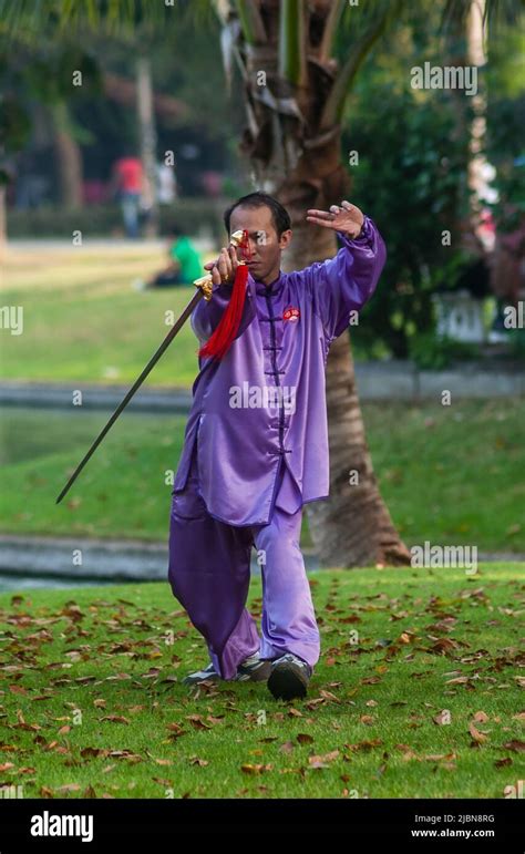 Thai Mature Man Undertaking Tai Chi Exercises With A Long Blade Sword In Lumpini Park Bangkok