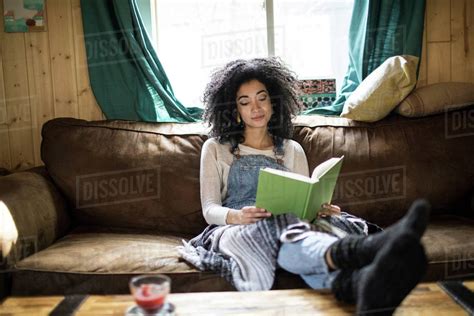 Young Woman Sitting On Sofa Reading Book Stock Photo Dissolve