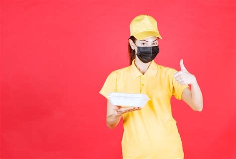 Free Photo Female Courier In Yellow Uniform And Black Mask Holding A Takeaway Package And