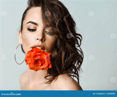 Portrait Of Young Beautiful Brunette Naked Woman In Circle Earrings With Rose In Hair Biting