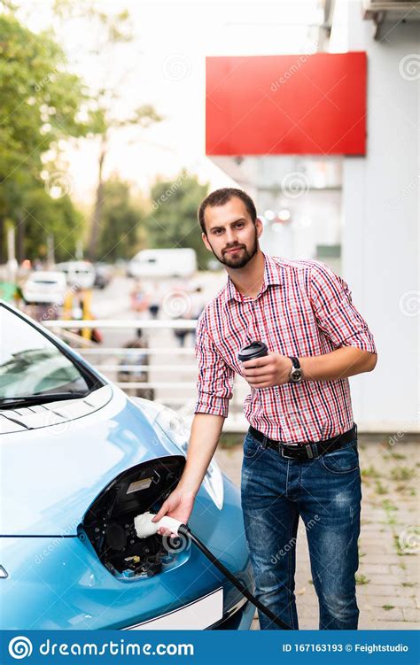 Young Man Charging His Electric Car And Drinking Coffee Stock Image