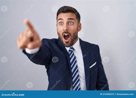 Handsome Hispanic Man Wearing Suit And Tie Pointing With Finger Surprised Ahead Open Mouth