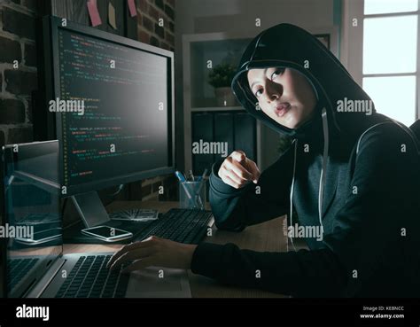 Young Female Computer Programmer As Hacker Doing Illegal Working Online And Looking At Camera