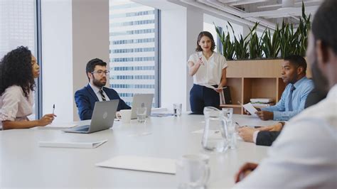 Businesswoman Standing Giving Presentation To Colleagues Sitting Around