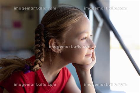 Portrait Of A Caucasian Schoolgirl With Blonde Hair In Plaits Wearing A Red T Shirt Sitting At