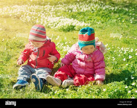 Little Boy And Girl In Hats Sitting On The Field With Soft Toys In