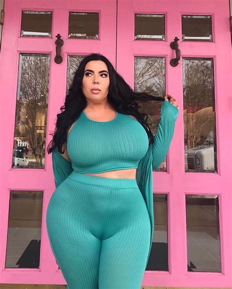 A Woman Posing In Front Of A Pink Door With Her Hands On Her Hips And