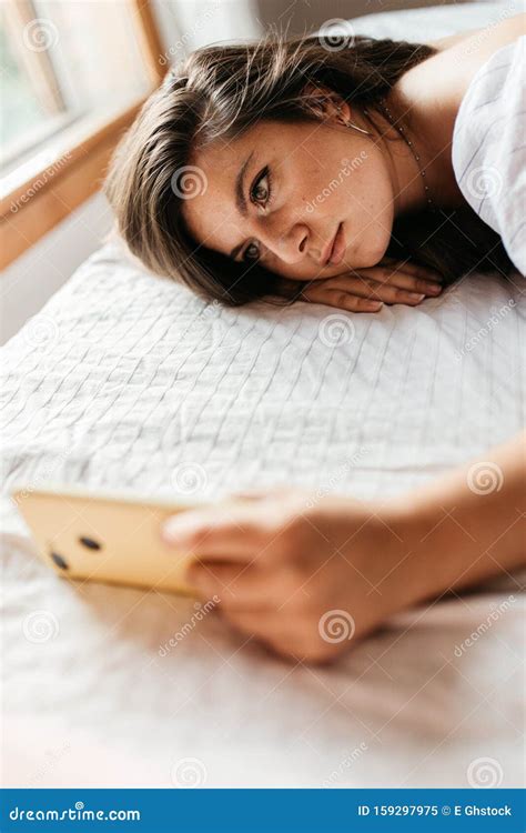 Close Up Portrait Of Young Sad Woman Lying On The Bed Looking At Her Smartphone Feels Unhappy