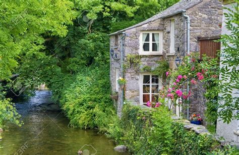An Old Quaint English Cottage On The Bank Of A Small River In