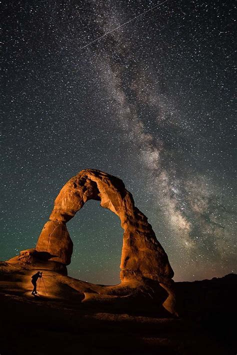 A Person Standing In Front Of An Arch Under The Night Sky With Stars