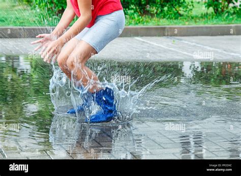 Girl In Rubber Boots Jumping In A Puddle After A Rain Outdoor On Summer