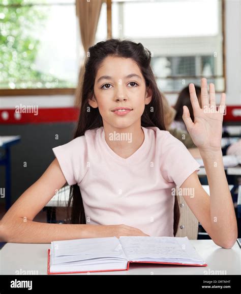 Schoolgirl Raising Hand In Classroom Stock Photo Alamy