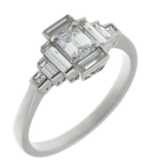 A 1920's art deco style ring with an octagon shaped, emerald cut emerald main stone and baguette cut diamond stepped shoulders. Art deco emerald cut and baguette diamond cluster ring