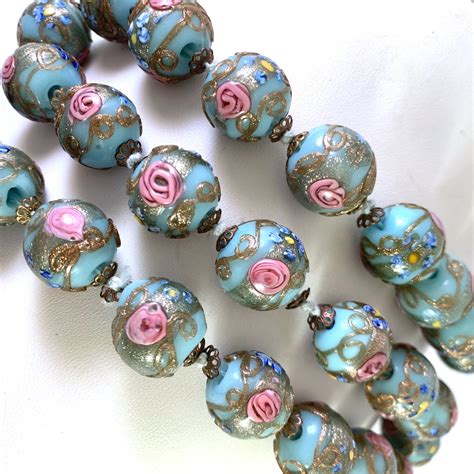 A Bunch Of Beads That Are Sitting On A White Tablecloth With Pink And Blue Flowers