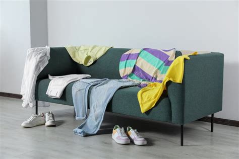 Messy Pile Of Clothes On Sofa And Shoes In Living Room Stock Photo