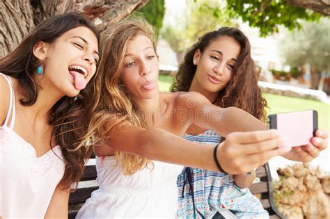 Två Tonårs Flickor Som Sitter På Bänken Som Tar Selfie Parkerar in