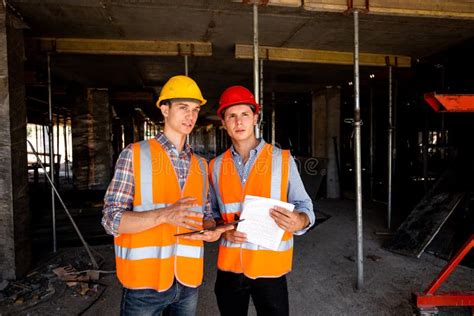 Two Young Civil Engineers Dressed In Orange Work Vests And Helmets Work