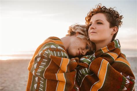 content lesbian couple wrapped in a blanket at the beach stock image image of real lifestyle