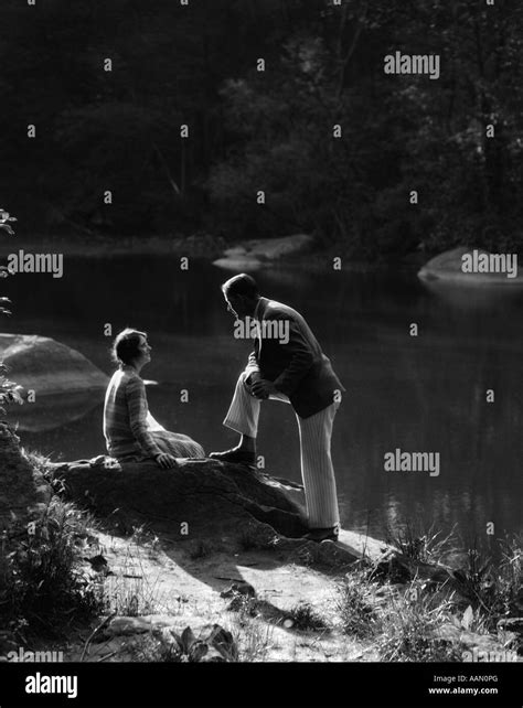 1920s 1930s Woman Sitting On Rock Lakeside Talking To Man Standing With Foot On Rock Leaning On