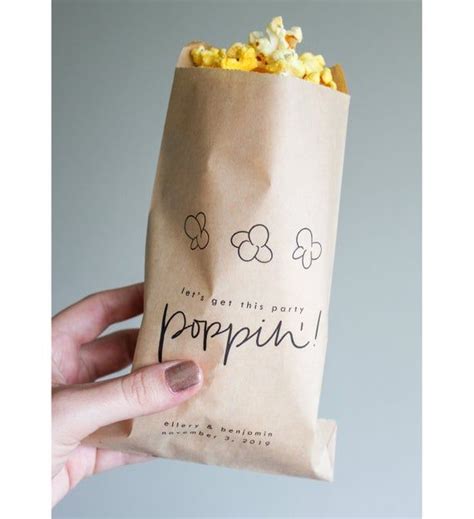 A Hand Holding A Brown Paper Bag With Popcorn In It And The Words Poppin Written On It