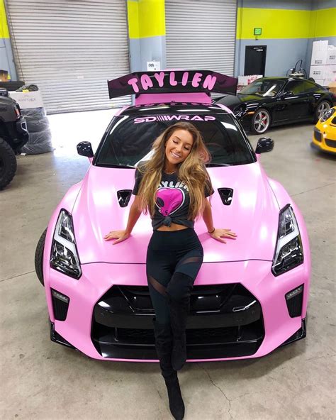 A Woman Sitting On The Hood Of A Pink Sports Car With Her Hands On Her Hips