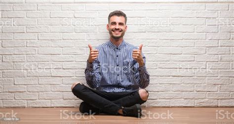Üzerinde beyaz tuğla duvar başarı işareti el ile olumlu hareketi yaparken oturan genç yetişkin