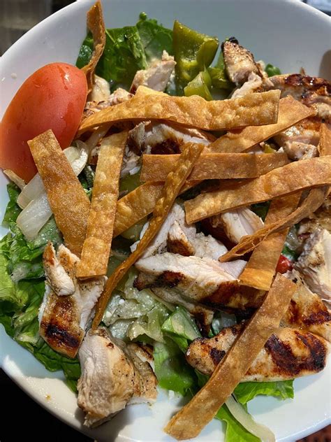 a salad with chicken lettuce and tomatoes in it on a white plate
