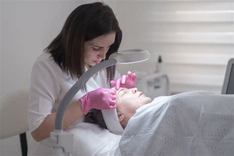 Cosmetologist Examines Client Skin Through Magnifying Lamp During A