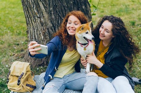 Happy Girls Friends Taking Selfie In Park With Cute Dog Using