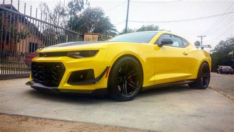 A Yellow Chevrolet Camaro Parked In Front Of A Fence