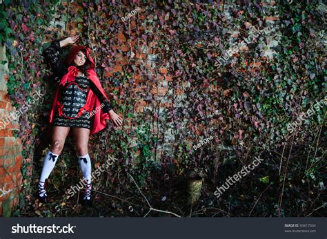 Attractive Scared Girl In Red Hood Leaning On Brick Wall