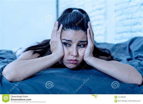 Sad And Depressed Portrait Of Latin Woman On Bed With White Back Stock