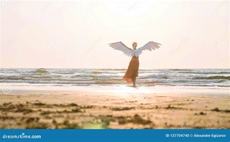 Beautiful Female Angel Walking Barefoot Toward The Sea At Sunset Stock