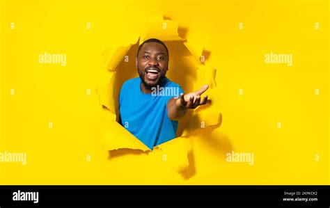 happy black man stretching open palm holding invisible object posing through hole in torn