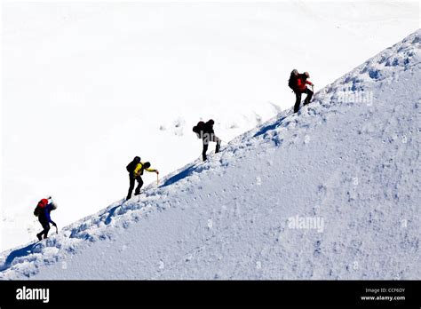 Mountain Climbers Ascending Ice Covered Ridge In Snow Near Summit Of