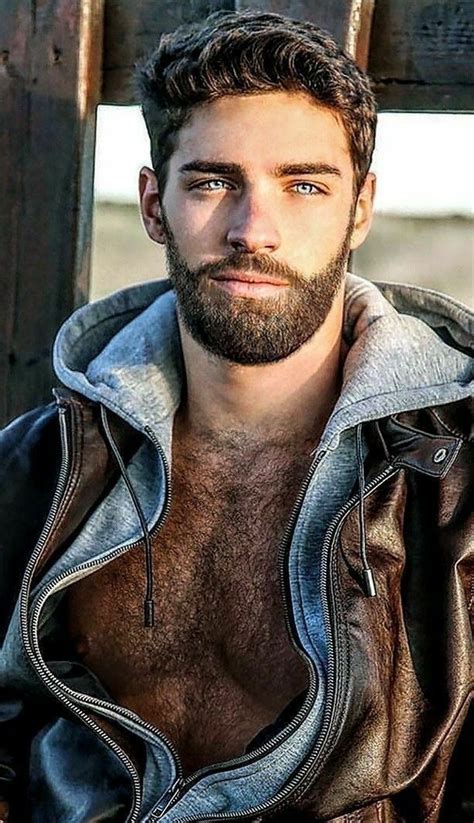 a man with a beard and no shirt is posing for the camera wearing a leather jacket