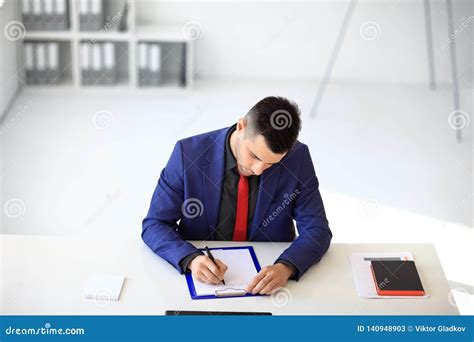 Businessman Signing Document Sitting At His Desk In The Office Stock