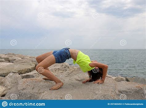 Girl Performs Gymnastic Exercises Arching Her Back Backwards On The Rocks By The Sea Without