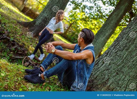 Man Sitting Under Tree And Looking At His Girlfriend Stock Photo