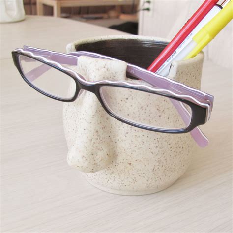 a pair of glasses sitting on top of a white cup with some pencils in it