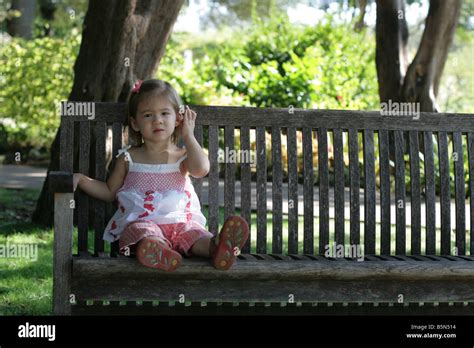 a 2 year old girl tugs at her ear while sitting outside on a park bench on a sunny day stock