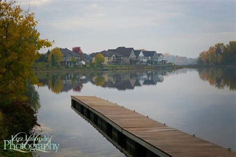 A Wooden Dock Sitting On Top Of A Lake Next To Houses In The Fall Time